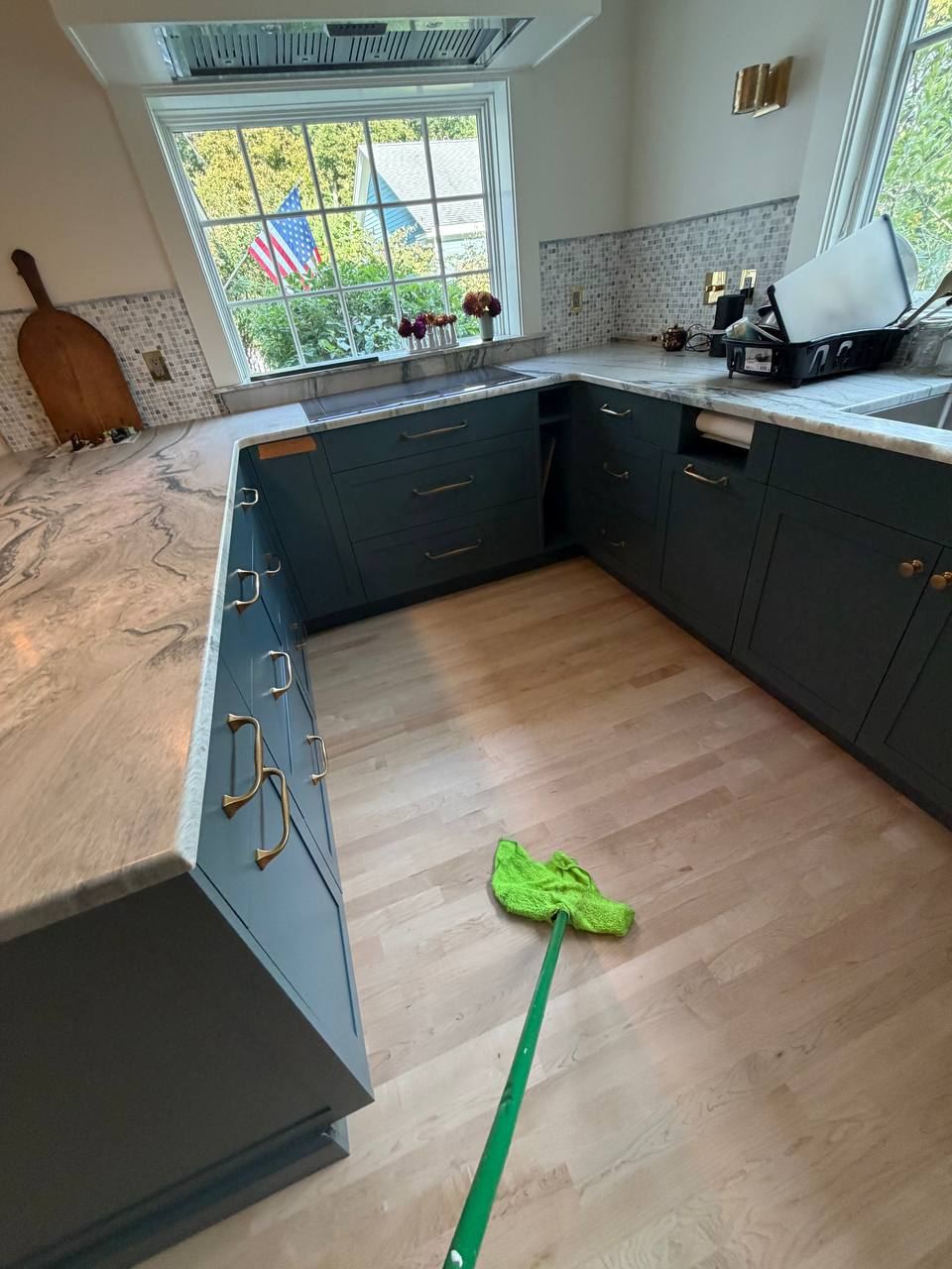 Prime Cleaning Solutions team mopping a bright kitchen with green cabinets and hardwood floors